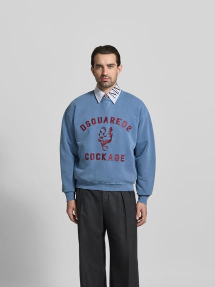 Männermodel trägt Regular Fit Sweatshirt mit Logo-Detail von Dsquared2, reine Baumwolle, Rundhalsausschnitt, elastische Abschlüsse, Ganzkörperansicht von vorne.