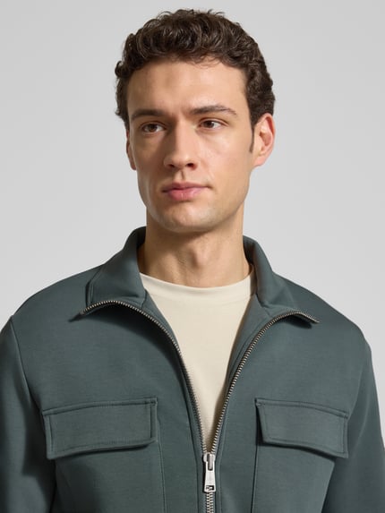 Mężczyzna nosi Regular Fit Sweatjacke aus Baumwoll-Mix von Marc O'Polo, bawełniany scuba materiał, kolor jednolity, dwie kieszenie na piersi, długi rękaw, stójka, zamek dwukierunkowy, label patch; zbliżenie na górną część ciała, widok z przodu.