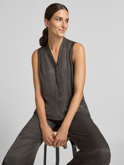 Frauenmodel trägt Regular Fit Blusentop aus reiner Viskose Modell 'Zenaya' von someday, satinierte dunkelgraue Oberfläche, Nahaufnahme Oberkörper.