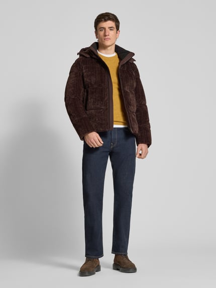 Männermodel trägt Pufferjacke mit abnehmbarer Kapuze von BOSS Orange aus Cord mit Struktur, Reißverschlüssen, Stehkragen, Ganzkörperansicht von vorne