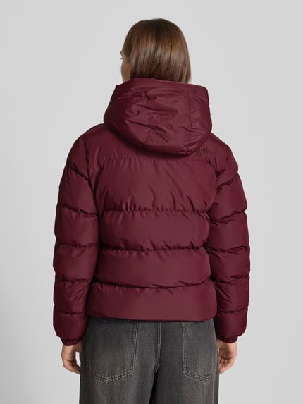 Frauenmodel trägt Regular Fit Jacke in Stepp-Optik von Superdry, bordeauxrot, glatte Textur, Kapuze, Rückenansicht, Kontext: Damen Jacke von Superdry, Stepp-Optik, Regular Fit, Kapuze mit Tunnelzug, Reißverschluss, Rückenlänge Größe S 58 cm, Schulterbreite 46 cm, Brustweite 52 cm, Ärmellänge 64 cm. Ganzkörperansicht Rückansicht