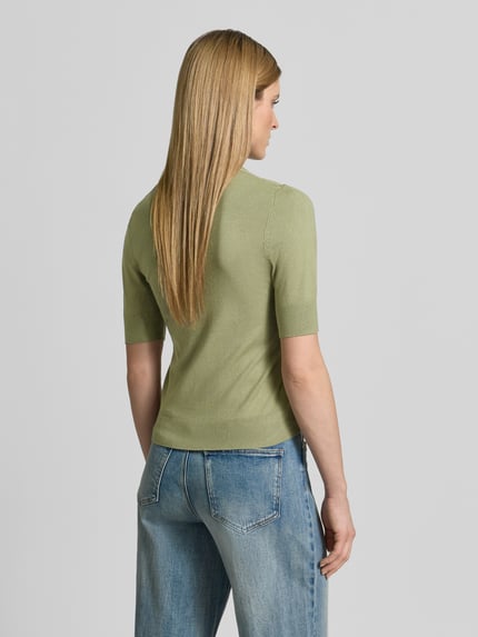 Frauenmodel trägt Slim Fit T-Shirt aus Viskose-Mix von s.Oliver RED LABEL in Strickoptik, grün, Feinstricktextur, Ganzkörperansicht Rückansicht.