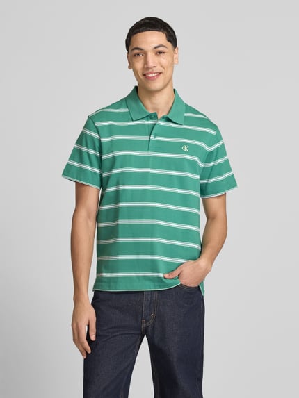 Męski model nosi Regular Fit Poloshirt mit Logo-Stitching von Calvin Klein Jeans z bawełny, kołnierzyk polo, listwa guzikowa, długość tyłu 69 cm, widok całej sylwetki od przodu.