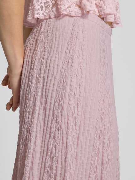 Kobiece model prezentuje długa spódnica Maxirock mit Spitze und elastischem Bund von Gina Tricot, mieszanka materiałów z dodatkiem streczu, linia a, koronka, elastyczny pas, kolor jasnoróżowy, tekstura koronkowa i plisowana, szerokość w rozmiarze S: 33 cm, całkowita długość: 101 cm, detailaufnahme.