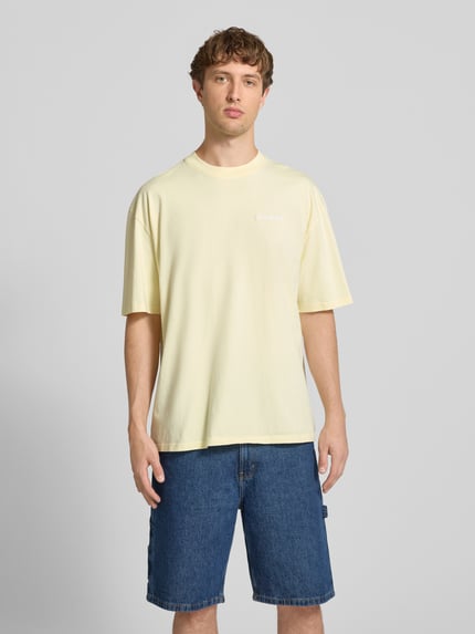 Männermodel trägt Oversized T-Shirt mit Label-Stitching von Pegador, hellgelb, Baumwoll-Mix, Rundhalsausschnitt, Ganzkörperansicht von vorne. Herren T-Shirt, Rückenlänge bei Größe M: 70 cm.