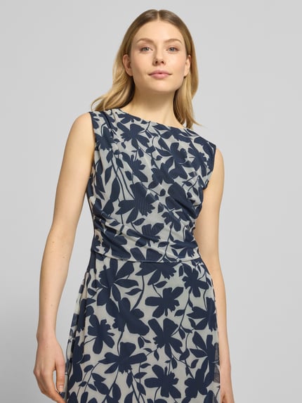 Frauenmodel trägt Regular Fit Midikleid mit floralem Allover-Print von Swing, Elastischer-Material-Mix, Rundhalsausschnitt, Ärmelloses-Design, Nahtreißverschluss, Raffung, taillierte Passform, blickdichter Unterrock, florale Muster in Blau auf hellem Grund, Nahaufnahme Oberkörper.