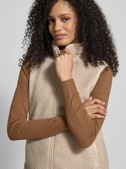 Frauenmodel trägt Fleeceweste mit Stehkragen Modell 'SIV' von Didriksons, Regular-Fit, Reißverschluss, beige Textur, Nahaufnahme Oberkörper. Rückenlänge 67 cm, Schulterbreite 38 cm, Brustweite 48 cm bei Größe 36.