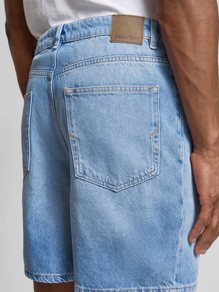 Mężczyzna nosi Loose Fit Jeansshorts aus Baumwoll-Lyocell-Mix Modell 'ALEX' von SELECTED HOMME, jasny denim, etykietka z logo, 5 kieszeni, widok całej sylwetki z tyłu