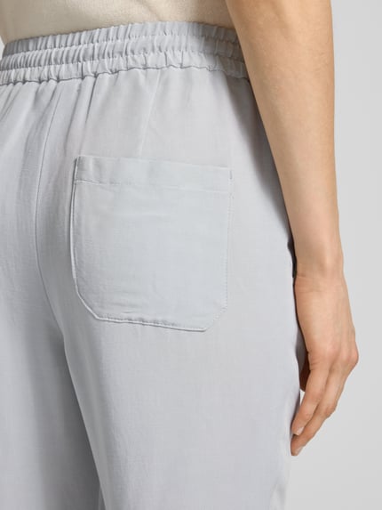 Vrouwenmodel draagt Straight Fit stoffen broek uit viscosemix met linnenlook van Marc Cain, steekzakken, elastische band met tunnelkoord, detailopname rug.