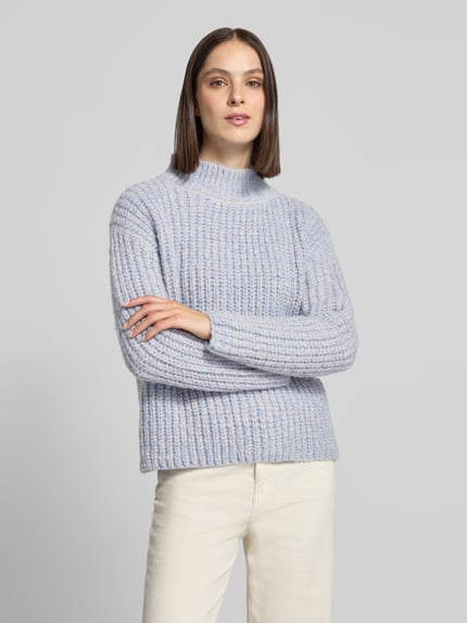 Frauenmodel trägt Grobstrickpullover mit Stehkragen von Apricot in Hellblau, relaxed Fit, strukturierte Textur, Ganzkörperansicht von vorne.