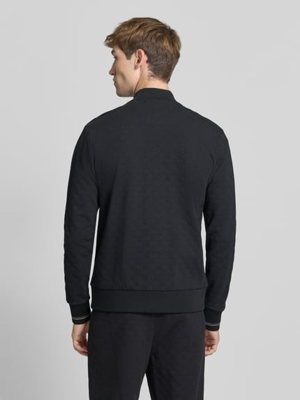 Männermodel trägt Regular Fit Sweatjacke aus Baumwoll-Mix Modell 'SW_Revival Skarley' von BOSS, schwarz mit Strukturmuster, gerippte Abschlüsse, Reißverschluss, Logo-Schriftzug, Ganzkörperansicht Rückansicht.