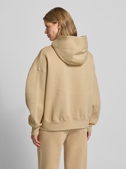 Frauenmodel trägt Oversized Hoodie mit Logo von Nike aus Baumwoll-Mix in Beige mit Känguru-Tasche, Ganzkörperansicht Rückansicht.