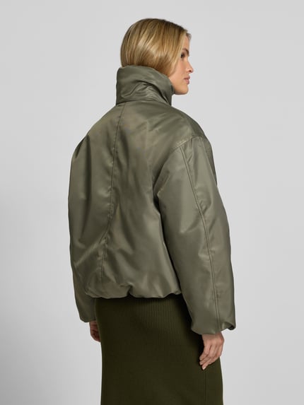 Frauenmodel trägt Bomberjacke mit Stehkragen Modell 'CYRUS' von Anine Bing, oliv, unifarben, cropped Länge, reine Baumwolle, Ganzkörperansicht Rückansicht.
