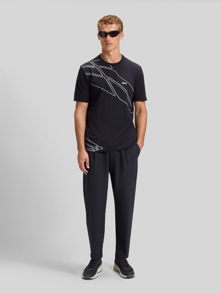 Männermodel trägt Tapered Bundfaltenhose mit halbelastischer Bund Modell 'CONVERT-PLEAT' von BOSS Green, unifarben, Ganzkörperansicht von vorne.
