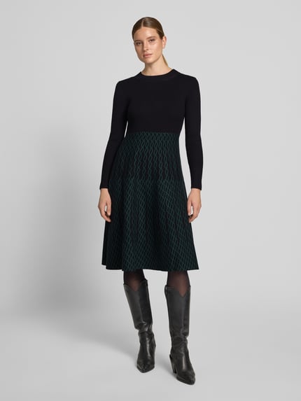 Vrouwenmodel draagt Knielanges Kleid mit Rundhalsausschnitt van Apricot, zwarte top, groene rok met patroon, viscosemix, getailleerd model, knielengte, ruglengte maat S 107 cm, borstwijdte maat S 35 cm, mouwlengte maat S 63 cm, geheel van voren te zien.