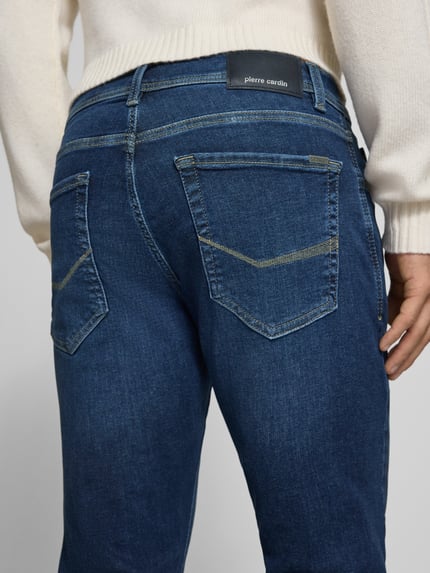 Männermodel trägt Regular Fit Jeans im 5-Pocket-Design Modell 'Lyon' von Pierre Cardin in Dunkelblau, Detailaufnahme Rückansicht, elastischer Baumwoll-Mix mit Lyocell-Anteil, sichtbares Label am Bund, Kontext: Herren Jeans, Knopf- und Reißverschluss, Bundweite 41 cm, Innenbeinlänge 79 cm.