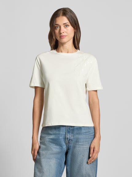 Frauenmodel trägt Regular Fit T-Shirt aus reiner Baumwolle mit Blumen-Applikation von Christian Berg Woman, kurzärmelig, weiß, Ganzkörperansicht von vorne.