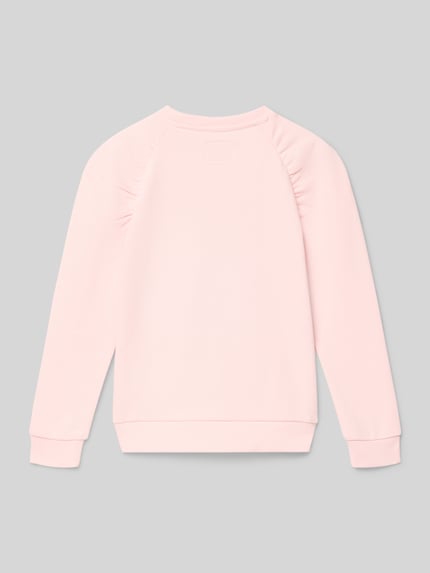 Mädchen trägt Bluza z detalem z logo Sweatshirt mit Label-Detail od Guess, bawełna, krój regular fit, prążkowane wykończenia, okrągły dekolt, różowy kolor, całkowity widok z tyłu.