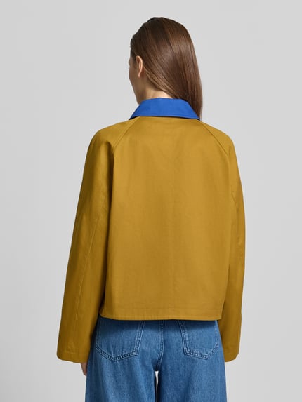 Frauenmodel trägt Kurze Barn-Jacket mit Kontrast-Kragen - curated by Tinvcb von SIC, senfgelb mit blauem Umlegekragen, Relaxed Fit aus reiner Baumwolle, Rückenlänge 56 cm, Schulterbreite 44 cm, Brustweite 60 cm, Ärmel 57 cm, Ganzkörperansicht Rückansicht.