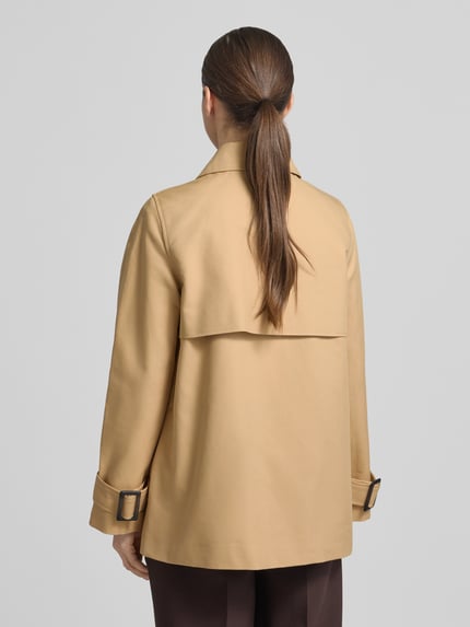 Frauenmodel trägt Trenchcoat mit Ärmelriegeln von Stefanel aus reiner Baumwolle in Beige, Zweireiher, ganzkörper Rückansicht.