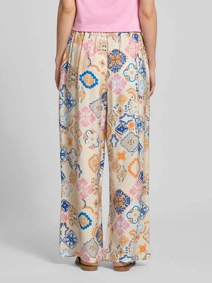 Vrouwenmodel draagt Wide Fit Stoffhose aus Viskose-Mix Modell 'Lancie' van ICHI met bloemrijke alloverprint in beige, blauw en roze, elastische tailleband, damestextuur met linnen, context: viscosemix met linnen, binnenbeenlengte 73 cm, taillewijdte 38 cm, Ganzkörperansicht Rückansicht.