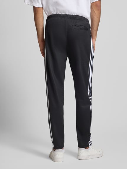 Männermodel trägt Trainingshose mit Label-Stitching Modell 'BECKENBAUER' van adidas Originals in zwart-wit, katoenmengsel, rugaanzicht.