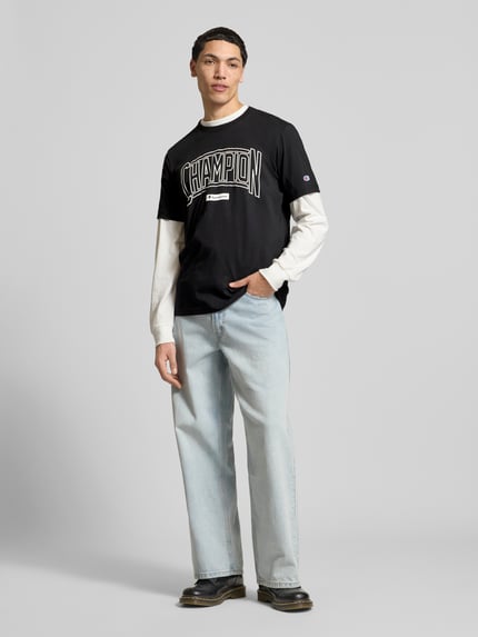 Mannelijk model draagt T-shirt met logo en ronde hals van CHAMPION, puur katoen, regular fit, labelstitching, ruglengte maat M 70 cm, voorkant volledige lichaamsopname.
