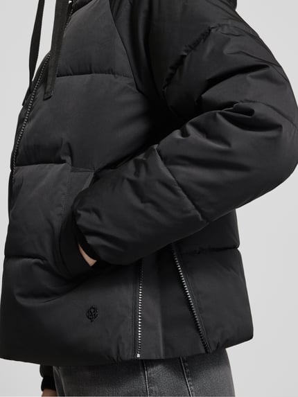 Vrouwenmodel draagt Regular Fit Steppjacke aus Material-Mix Modell 'Pavinaria' van MSCH Copenhagen, zwart, detailopname, context: dames steppjacke, materiaal-mix, kap met trekkoord, ritssluiting, steekzakken, ruglengte maat XS/S 60 cm, schouderbreedte 48 cm, borstwijdte 52 cm, mouwlengte 59 cm.