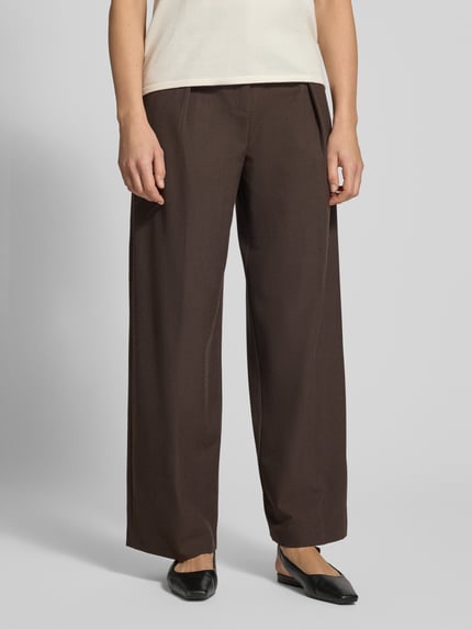 Frauenmodel trägt Bundfaltenhose aus Viskose-Mix Modell 'LEO' von MANGO, Braun, Relaxed Fit, Detail Gesäßtaschen, Ganzkörperansicht von vorne.