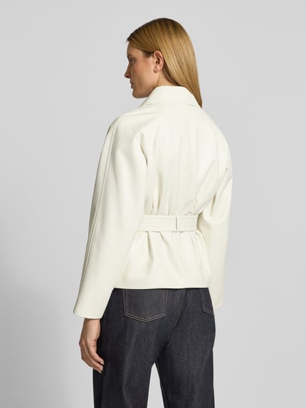 Frauenmodel trägt Regular Fit Kunstlederjacke mit Bindegürtel Modell 'AISANDI' von HUGO in unifarbenem Weiß mit Reverskragen, Glattledertextur, Ganzkörperansicht Rückansicht.