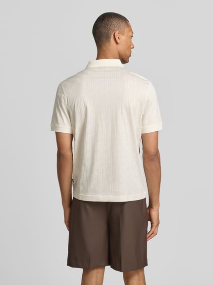 Mężczyznamodel nosi Modern Fit koszulkę polo z fakturowanym wzorem model 'Roberto' od JOOP! kolekcja, czysta bawełna, kołnierzyk polo, krótka listwa guzikowa, detal z logo, długość tyłu w rozmiarze M: 68 cm, widok całej sylwetki z tyłu.