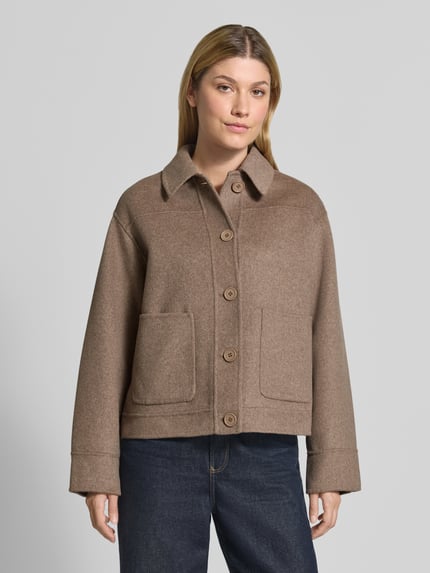 Kobiece model nosi Hemdjacke aus Woll-Mix mit Eingrifftaschen od Smith and Soul, mieszanka wełny, prosty krój, kołnierzyk typu kent, listwa guzikowa, naszywane wpuszczane kieszenie, długość tyłu w rozmiarze S: 58 cm, szerokość ramion w rozmiarze S: 44 cm, szerokość w rozmiarze S: 60 cm, długość rękawów w rozmiarze S: 57 cm, odcienie brązu, gładka tekstura, widok całej sylwetki z przodu.
