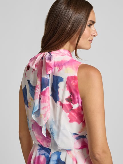 Vrouwenmodel draagt cocktailjurk met asymmetrische zoom van Vera Mont in kleurrijk bloemenpatroon, opstaande kraag, druppelvormige hals met strik en rugritssluiting, getailleerd model, midi-jurk, ruglengte maat 36: 112 cm, borstwijdte maat 36: 40 cm. Detailopname rug.
