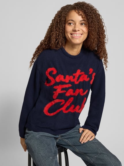 Frauenmodel trägt Pullover mit Santa Schriftzug von ONLY in mehrfarbiger Strickoptik, Motiv-Print, Rundhals, Ganzkörperansicht von vorne.