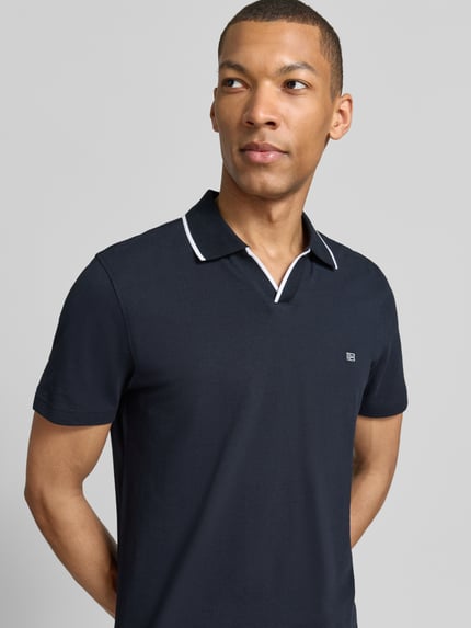 Männermodel trägt Modern Fit Poloshirt mit Logo-Stitching von Christian Berg Men in donkerblauw, katoen, polokraag, logo-detail, nahaufnahme oberkörper.