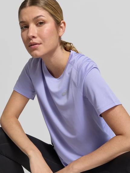 Frauenmodel trägt T-Shirt mit Rundhalsausschnitt und Logo-Print von ASICS in Flieder, gerader Schnitt, glatte Textur, Nahaufnahme Oberkörper, Damen T-Shirt von ASICS, leicht abgerundeter Saum, Rückenlänge bei Größe S 60 cm.