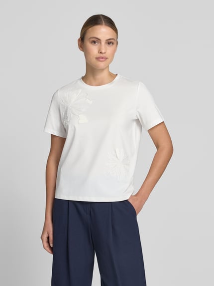 Vrouwenmodel draagt T-Shirt met Stitchings en Rundhalsausschnitt van Jake*s Collection, wit katoenmix, regular fit, ronde hals, ruglengte 56 cm bij maat S, bloemenstiksels op voorzijde, totaalbeeld van voren.