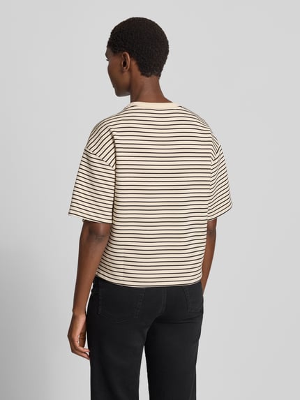 Männermodel trägt Oversized Fit T-Shirt aus Viskose-Mit von MSCH Copenhagen, beżowe z czarnymi paskami, mieszanka wiskozy, okrągły dekolt, krój oversized fit, rękaw o dł. 1/2, długość tyłu w rozmiarze XS/S: 54 cm, widok całej sylwetki z tyłu.
