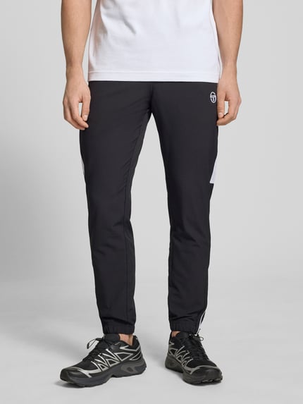 Männermodel trägt schwarze Sweatpants mit Logo-Stitching Modell 'CASPIO' von SERGIO TACCHINI, Material-Mix mit Stretch-Anteil, Körpernaher-Schnitt, Elastischer Bund mit Kordelzug, Seitliche Eingrifftaschen, Elastische Abschlüsse, Ganzkörperansicht von vorne.