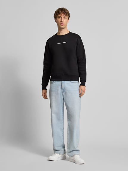 Männermodel trägt Regular Fit Sweatshirt aus Baumwoll-Mix mit Label-Detail von Alpha Industries, schwarze Farbe, elastische Abschlüsse, Ganzkörperansicht von vorne.