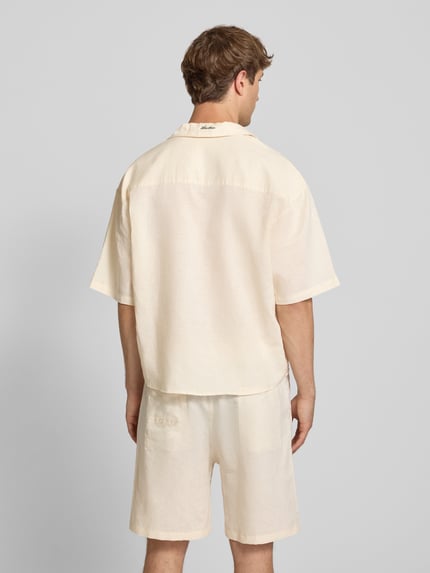 Männermodel trägt Relaxed Fit Leinenhemd mit Label-Stitching von ANOTHER COTTON LAB in Beige, Struktur wirkt luftig, Ganzkörperansicht Rückansicht, reines Leinen, Reverskragen, Knopfleiste, Label-Detail, Rückenlänge 70 cm, Schulterbreite 43 cm, Ärmellänge 35 cm.