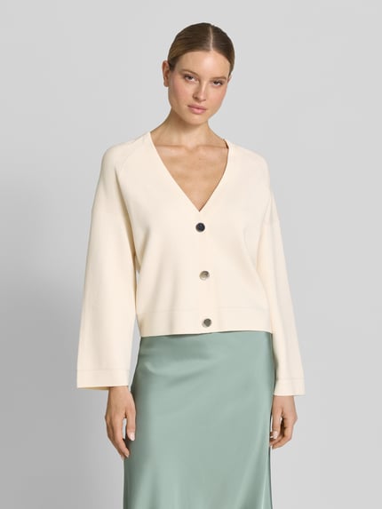 Frauenmodel trägt Strickjacke aus Viskose-Mix mit V-Ausschnitt von comma, cremefarben, Relaxed Fit, Knopfleiste, Ganzkörperansicht von vorne.