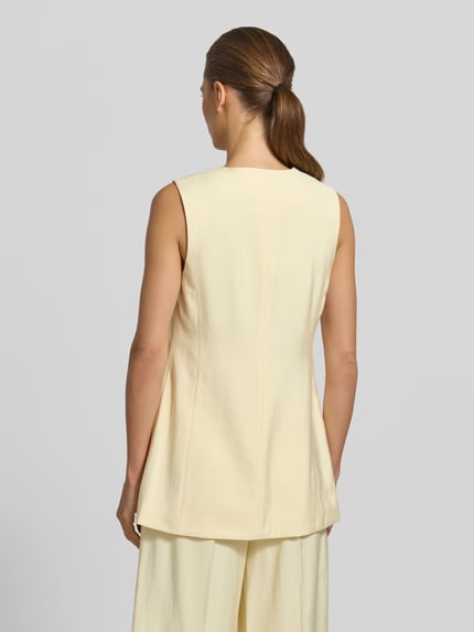 Vrouwenmodel draagt bodywarmer uit viscosemix van B.Young, getailleerd model, kleur lichtgeel, model 'ESSIE', klepzakken, ruglengte maat 36: 71 cm, schouderbreedte maat 36: 34 cm, borstwijdte maat 36: 41 cm, geheel beeld rugaanzicht