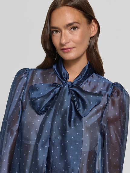 Frauenmodel trägt Schluppenbluse im semitransparenten Design von Rich & Royal in Dunkelblau mit Punkten, verdeckte Knopfleiste, Nahaufnahme Oberkörper.
