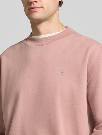 Männermodel trägt Sweatshirt mit Logo-Stitching Modell 'asher crew' von AllSaints in Rosa, Rippstruktur, Nahaufnahme Oberkörper.