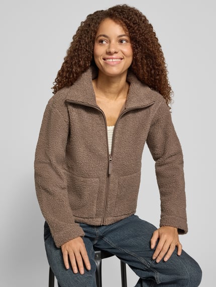 Frauenmodel trägt Teddyjacke mit hohem Stehkragen von ONLY in Braun mit grober Webpelztextur und Reißverschluss, Nahaufnahme Oberkörper. Damen Teddy- / Webpelzjacke von ONLY.