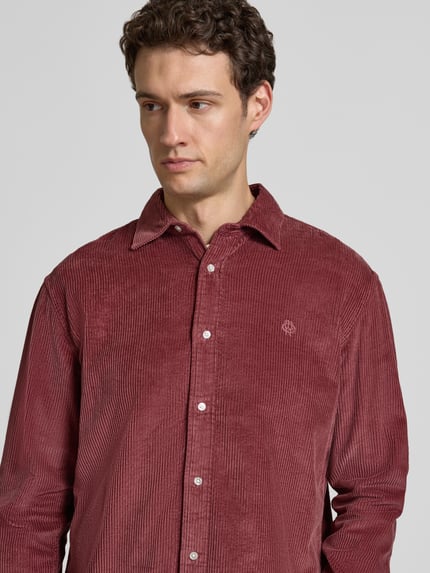 Männermodel trägt Regular Fit Freizeithemd mit Label-Stitching von MCNEAL aus rotem Cord, Kentkragen, reine Baumwolle, Nahaufnahme Oberkörper.