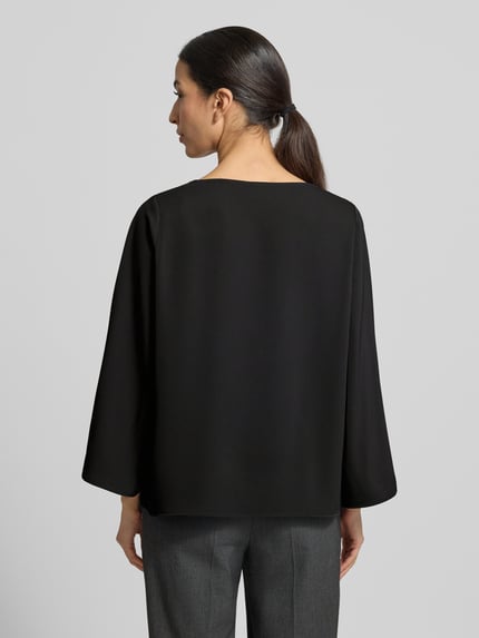 Modelka nosi Blusenshirt mit Rundhalsausschnitt von comma, czarny materiał z domieszką stretchu, luźny krój, długość tyłu 59 cm, długość rękawa 52 cm, widok całej sylwetki od tyłu.