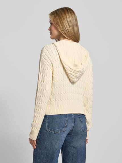 Vrouwenmodel draagt Comfort Fit Strickjacke aus reiner Baumwolle Modell 'CALICO' van Tommy Hilfiger, crème kleur, kabelpatroon, geribde manchetten, kapuchon, labeldetail, unifarben, langem mouw, achterkant totaalbeeld.