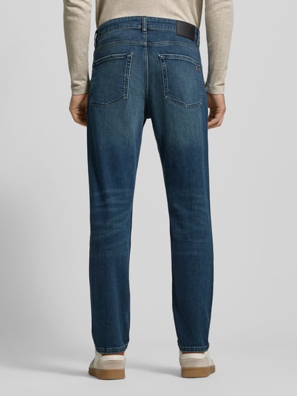 Männermodel trägt Slim Fit Jeans aus Baumwoll-Mix Modell 'SMU ONYX' von BOSS Orange, Denim-Optik, Label Patch, Rückansicht.
